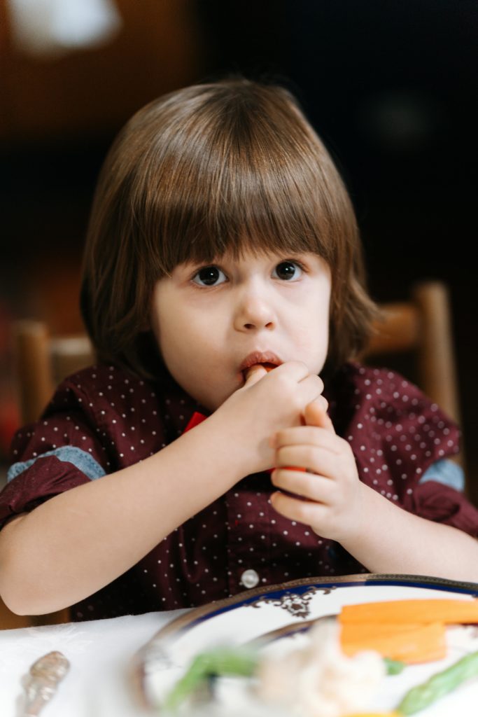Young child enjoying a meal at the table, featuring healthy vegetables, indoors.