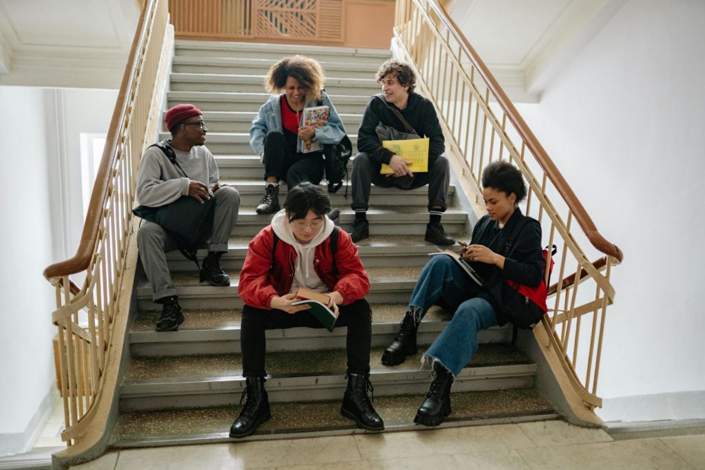A diverse group of college students sitting on stairs, studying and socializing indoors.